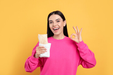 Happy young woman with delicious shawarma on yellow background