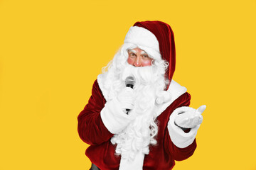 Fototapeta na wymiar Santa Claus singing with microphone on yellow background. Christmas music
