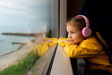 A girl in headphones on a train looks out the window. Journey.
