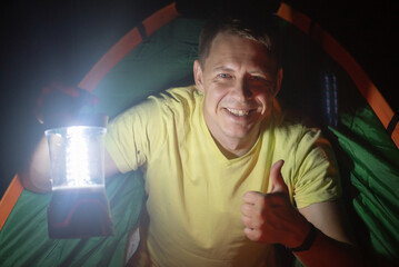 Happy smiling tourist with a flashlight is looking out from the tent.