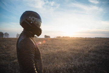  Tired motorcyclist walks on the field in the sunset rays.