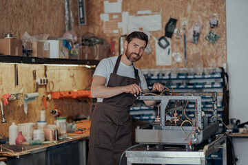 Portrait of repairman in uniform with broken coffee machine in workshop