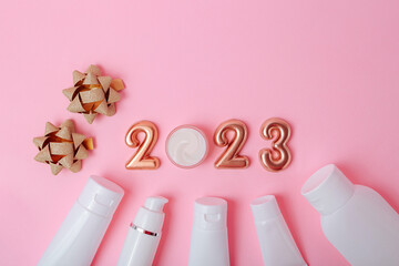 Top view of the cosmetics containers on pink background.Rose gold numbers 2023 above.Good for new year offer and text overlay.