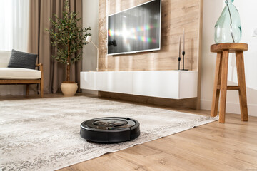 Black robotic vacuum cleaner in a new living room in light beige and gray colors - obrazy, fototapety, plakaty