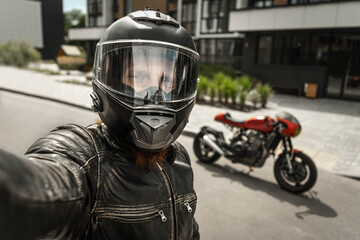 Biker in helmet takes a selfie in front of motorcycle