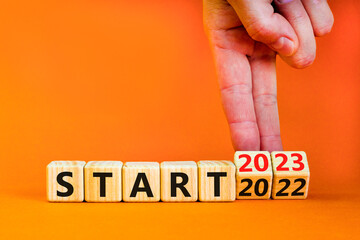 2023 start new year symbol. Businessman turns a wooden cube and changes words Start 2022 to Start 2023. Beautiful orange table orange background, copy space. Business 2023 start new year concept.