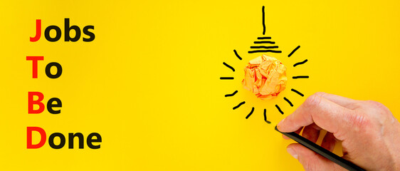 JTBD jobs to be done symbol. Concept words JTBD jobs to be done on yellow paper on a beautiful yellow background. Businessman hand. Light bulb. Business and JTBD jobs to be done concept. Copy space.