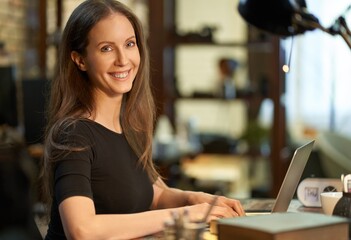 Successful confident businesswoman working, using laptop computer, looking at camera.