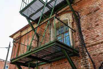 Old fire escape, emergency exit across the street. Brick wall and metal balcony on the facade of an...