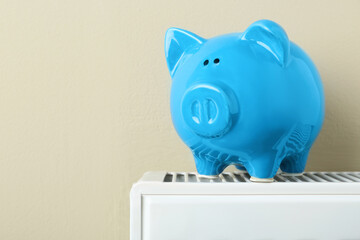 Piggy bank on heating radiator against beige background, space for text
