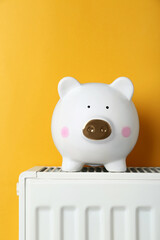 Piggy bank on heating radiator against orange background