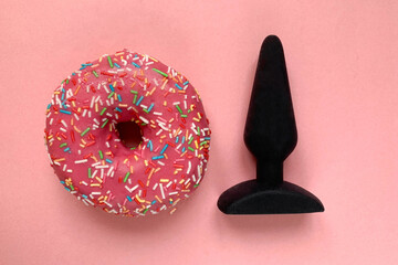 Sex toy and donut. Black butt plug on pink background
