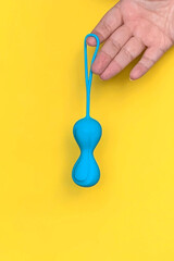 Sex toy. Blue geisha balls on a hand. Yellow background. Useful for sex shop, adult