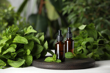 Bottles of mint essential oil and green leaves on white wooden table