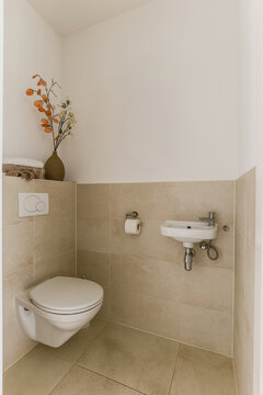 Wall hung toilet and small sink in corner in lavatory room with beige tile and whrite wall