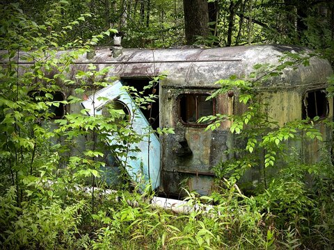 Abandoned Vintage Airstream Trailer RV In A Forest With Hanging Shoe Out Of One Of Its Windows