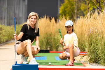 mother and daughter playing mini golf, children enjoying summer vacation - obrazy, fototapety, plakaty