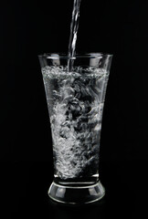 Pouring fresh water on glass on black background.