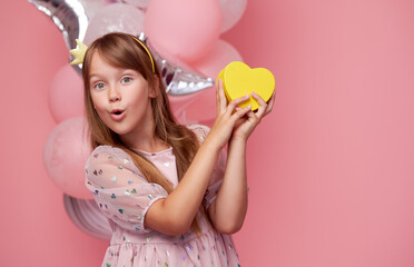 Obraz na płótnie Canvas Joyful child girl in elegant tulle dress near the balloons. Birthday present. Funny face celebrates birthday party on pink background.