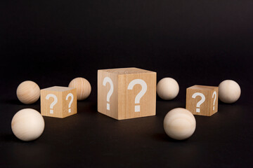 wooden cube with a question mark surrounded by wooden balls on a black table background