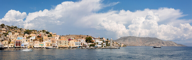 Fototapeta na wymiar Panoramic view, aerial skyline of small haven of Symi island. Village with tiny beach and colorful houses located on rock. Tops of mountains on Rhodes coast, Dodecanese, Greece . High quality photo