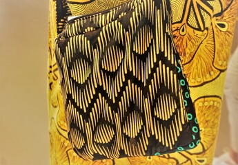 Gelbe-brauner Stoffbeutel mit Ethnomuster vor goldgelbem Kleid mit braunem afrikanischem Muster