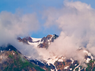 Rocky mountain peaks with snow in valleys framed by circle of clouds