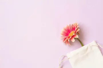 Gordijnen Pink gerbera flower came out from cloth pouch on lilac background. Horizontal background with space for text © Ken