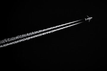 Twin-engined jetliner with contrails flying in black sky - obrazy, fototapety, plakaty