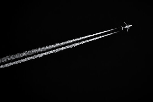 Twin-engined jetliner with contrails flying in black sky