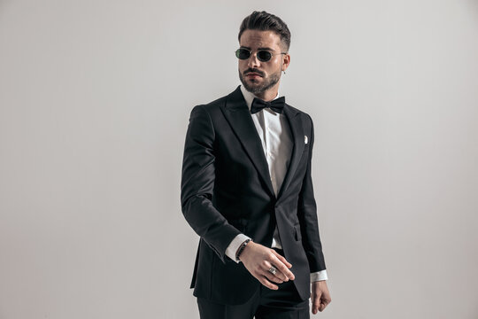 sexy elegant man in tuxedo wearing sunglasses and confidently posing