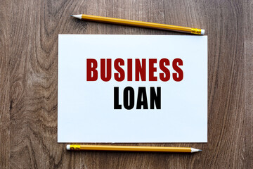 BUSINESS LOAN is written in a notebook which lies on a wooden table. Lettering on a business or financial theme. Business concept.