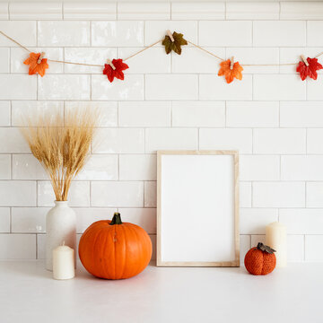 Autumn still life. Picture frame mockup, vase of wheat, orange pumpkins in cozy home room interior. Thanksgiving, Halloween, fall concept.