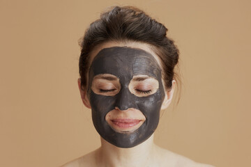 relaxed young woman with facial mask on beige background