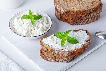 Fresh bread with carrots on a white wooden cutting board with curd cheese