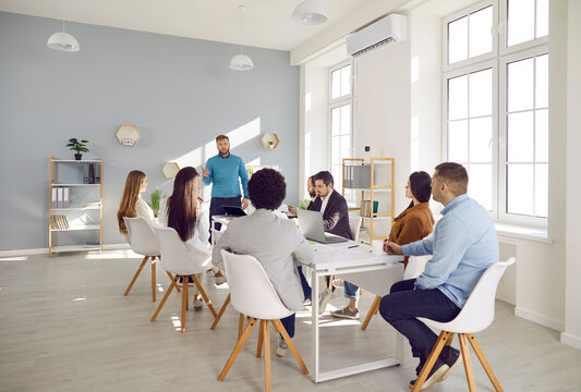 Confident male team leader or coach present company project to diverse employees at office meeting. Businessman hold lead briefing with multiracial businesspeople. Leadership concept.