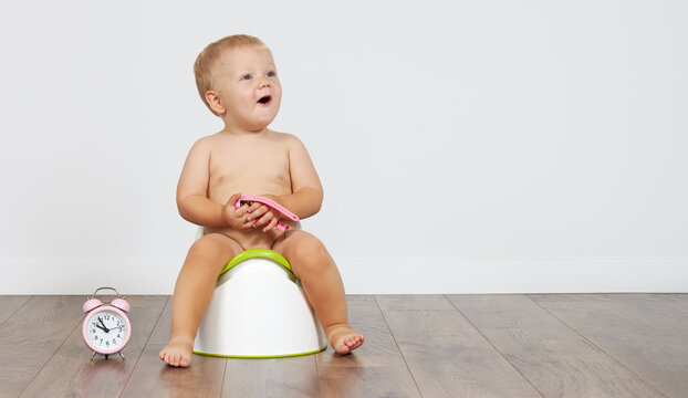 Cute baby boy sits on the potty with toilet paper in his hands. Potty training time