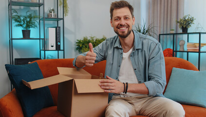 Portrait of happy adult man unpacking delivery parcel sitting at home. Smiling satisfied young guy shopper, online shop customer opening cardboard box receiving purchase gift by fast postal shipping