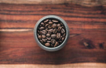 Roasted coffee beans in a cup on a wooden surface - top view