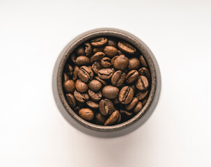 Roasted coffee beans in a cup on a white background - top view