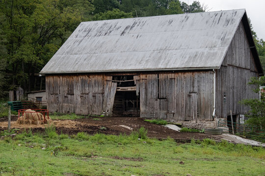 An old gray barn in rural Indiana. It is a grey overcast day with a barnyard in front. 