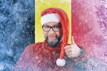 Portrait of handsome cheerful cheery bearded Santa red sweater on background flag of Belgium covered in frost, toned image