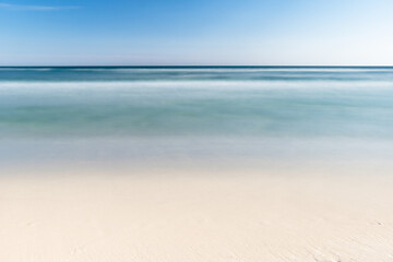 Long exposure of a beach on the Gulf of Mexico. The water is blue with golden sand and a blue sky. 