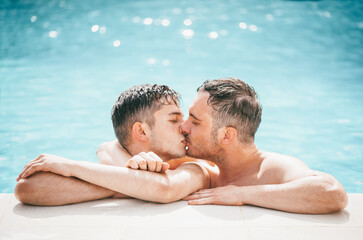 Gay couple relaxing in swimming pool. LGBT. Two young men enjoying nature outdoors, kissing and hugging. Young men romantic family in love. Happiness concept.