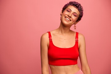 Fashion portrait of a woman with a short haircut of purple color and a smile with teeth in a red top on a pink background dancing happily