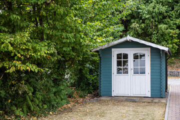 Cozy blue summer shed in green forest near bricks road, rural garden small house