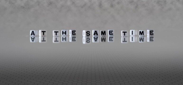 at the same time word or concept represented by black and white letter cubes on a grey horizon background stretching to infinity