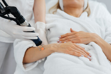 A young girl gets carbon peeling for the skin of her hands in a beauty salon. Laser pulses cleanse the skin. Hardware cosmetology. The process of photothermolysis, warming the skin.