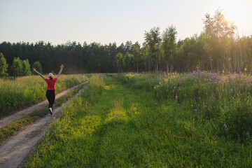 Back view of happy woman jogging outdoors at sunset and raising her hands up. The concept of healthy lifestyle and mental health.