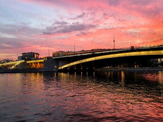 Beautiful embankment during sunset. Sunset on the river. Illuminated bridge across the river